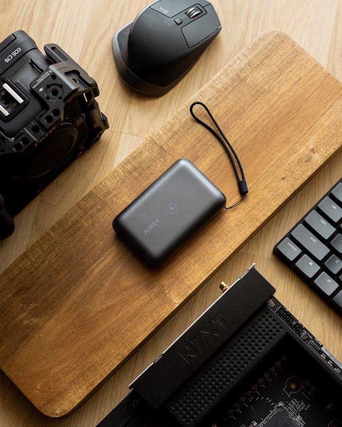 A stylish flat lay showcasing a camera, power bank, mouse, and keyboard on a wooden desk.